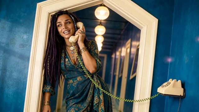 Ravenna laughs into a cream corded phone in an arched doorway, globe lights running down the blue corridor behind her, from A Little Bit Sideways