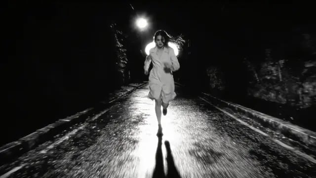 A runner in white races down a wet road under a street lamp in black and white, from Prey For Me, a trap metal music video by Pastor Fussycat